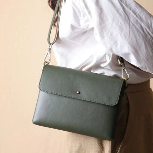 Side Profile of a Woman in a white shirt carrying a mint green leather crossbody shoulder side bag with a flap on her shoulder
