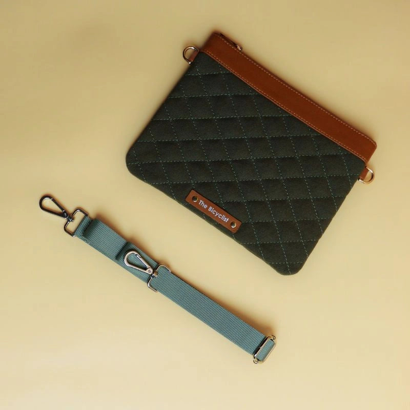 Flat Top view of a dark green cotton canvas quilted sling side bag with tan leather trims and dark green strap next to it