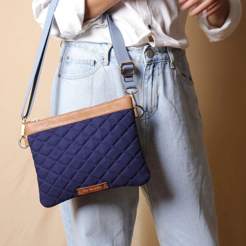 Woman holding a quilted deep blue canvas sling bag with tan trims