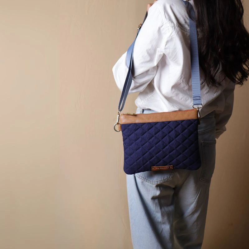 Woman in white shirt carrying a quilted deep blue canvas leather bag with tan trims