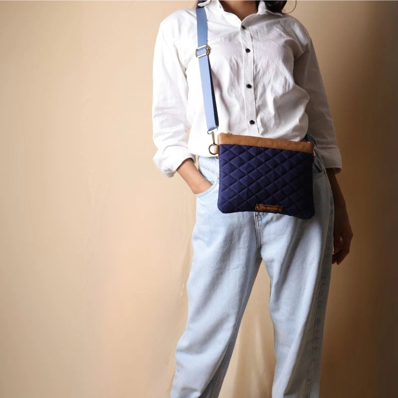 Woman in a white shirt carrying a crossbody deep blue canvas and tan leather sling bag across her shoulder