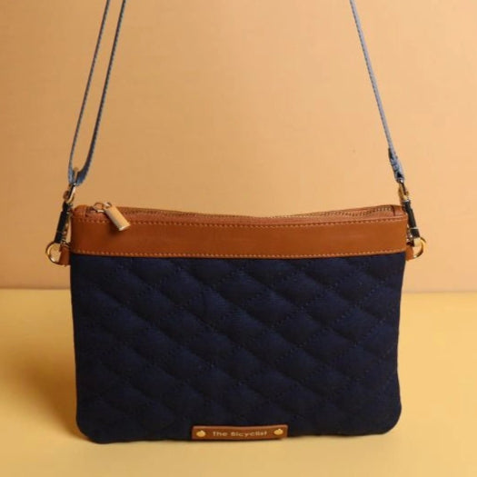 Upright view of a Deep Blue Quilted Canvas crossbody sling pouch bag in deep blue with tan leather trim and a golden zip closure