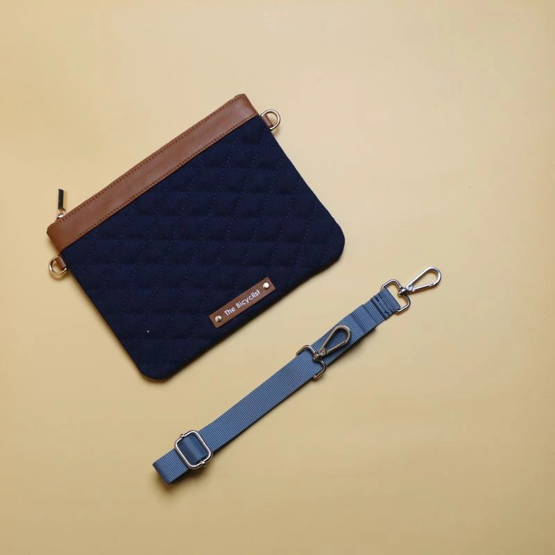 Top view of a deep blue quilted cotton canvas sling pouch bag with tan trims with its adjustable and removable strap next to it