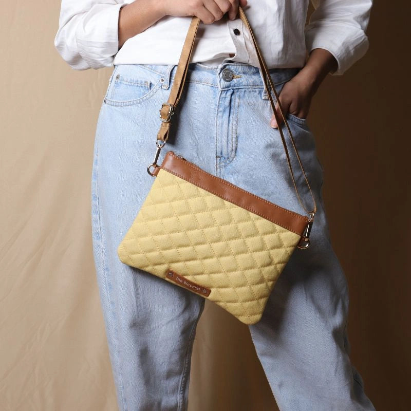 Woman in light blue denims holding a yellow quilted canvas and tan leather sling bag in her hand