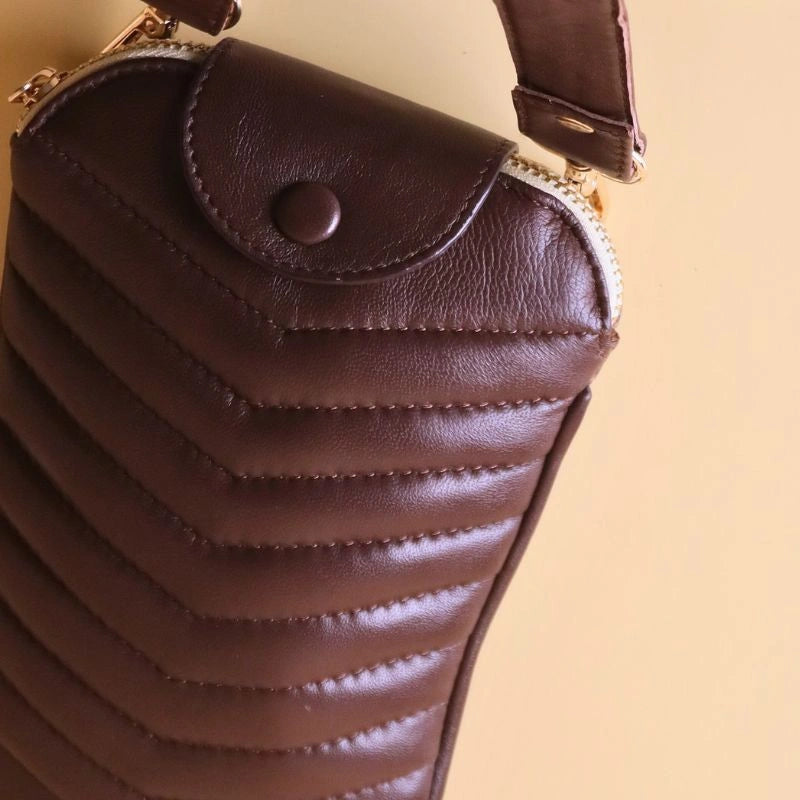 Detailed view of the the leather covered button and the golden zip of a dark brown quilted leather sling bag