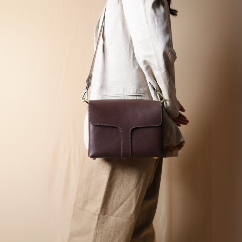 Woman in an off-white blazer carrying a dark brown leather crossbody sling bag with flap around the shoulder