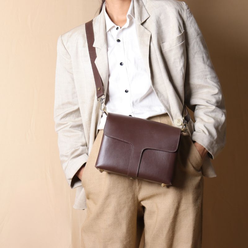 Front view of a woman in an off-white blazer carrying a dark brown leather crossbody sling bag with flap across her shoulder