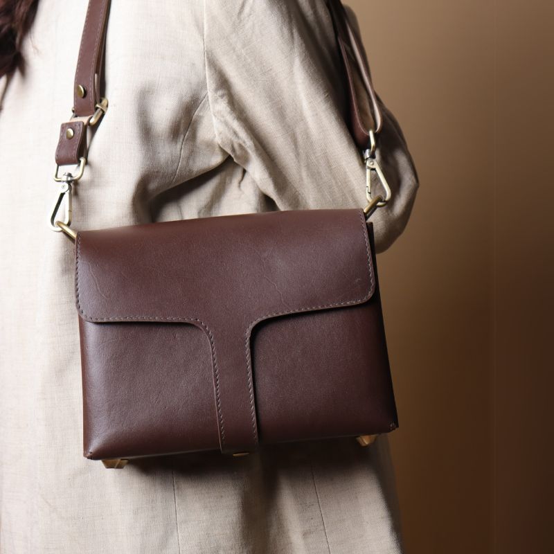 Back View of Woman in an off-white blazer carrying a dark brown leather crossbody sling bag with flap over her shoulder