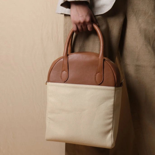 Woman in beige trousers carrying a top handle off-white white canvas and tan leather laptop work handbag