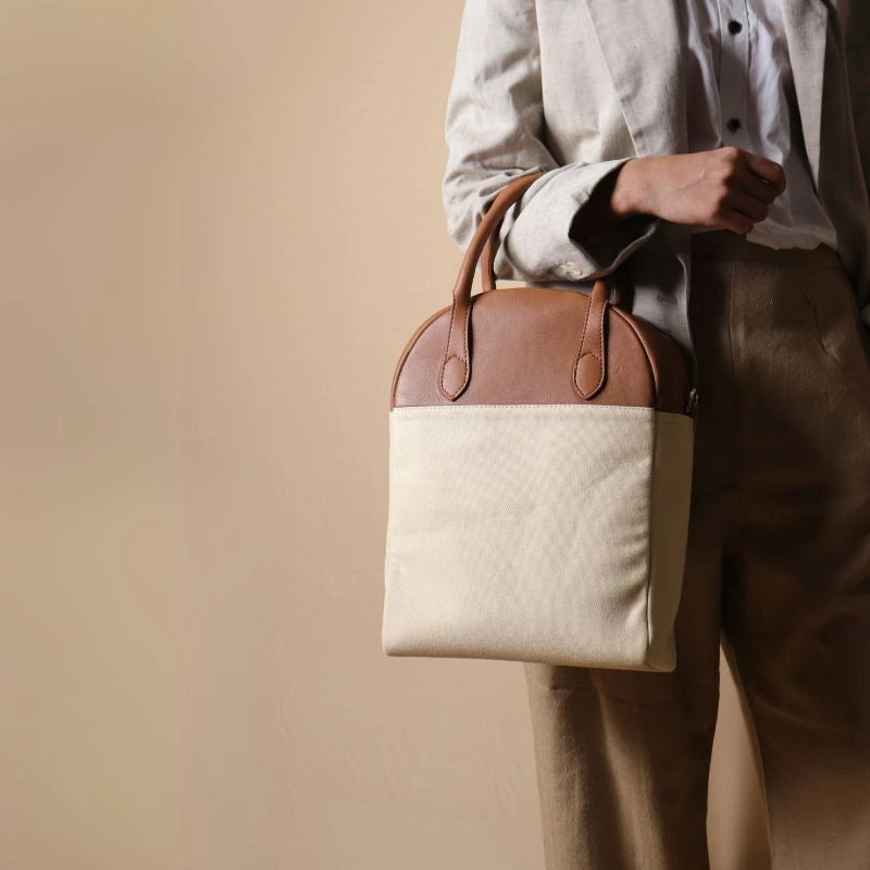 Woman in beige trousers and off white blazer carrying a top handle off-white white canvas and tan leather laptop work handbag