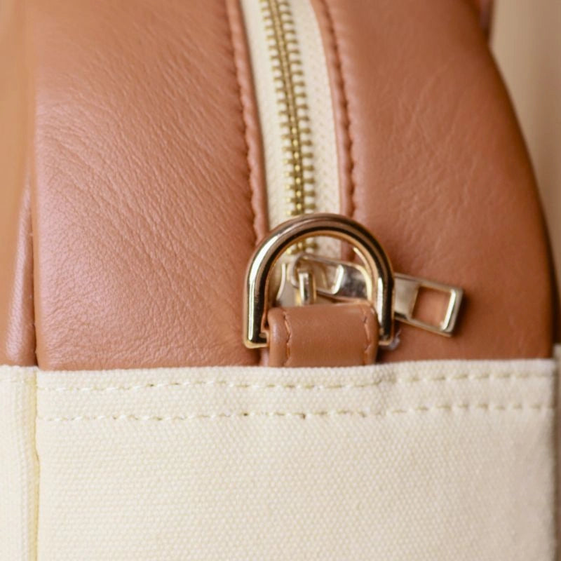 Detailed View of golden fittings with a gold metal zip of a off-white canvas and tan leather top handle work handbag