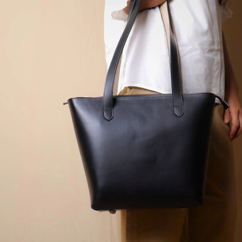 Black Leather Horizontal Tote Bag with zipped closure carried by a woman over her on her hand in a white shirt.