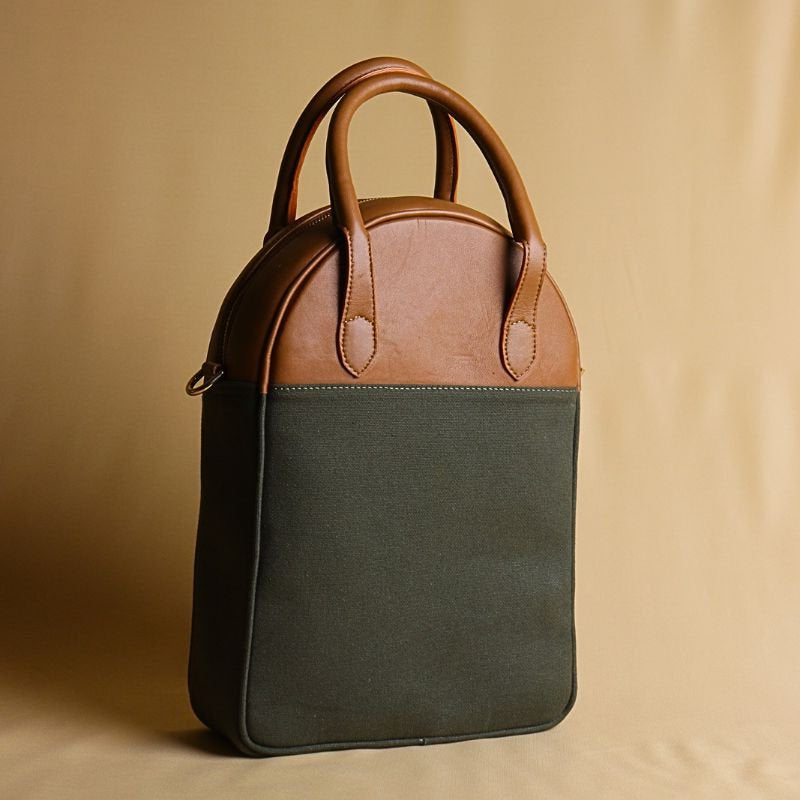 Hancrafted Canvas and Leather handbag-dark green canvas body with tan sheep leather top-beige felt lining-adjustable and removable white shoulder straps-front angle view-The Bicyclist