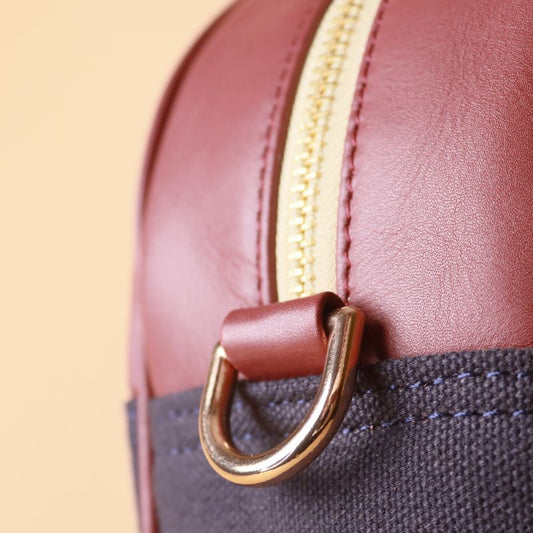 Hancrafted Canvas and Leather handbag-deep blue canvas body with maroon grain leather top-beige felt lining-adjustable and removable white shoulder straps-gold plated metal fittings-front detail view-The Bicyclist