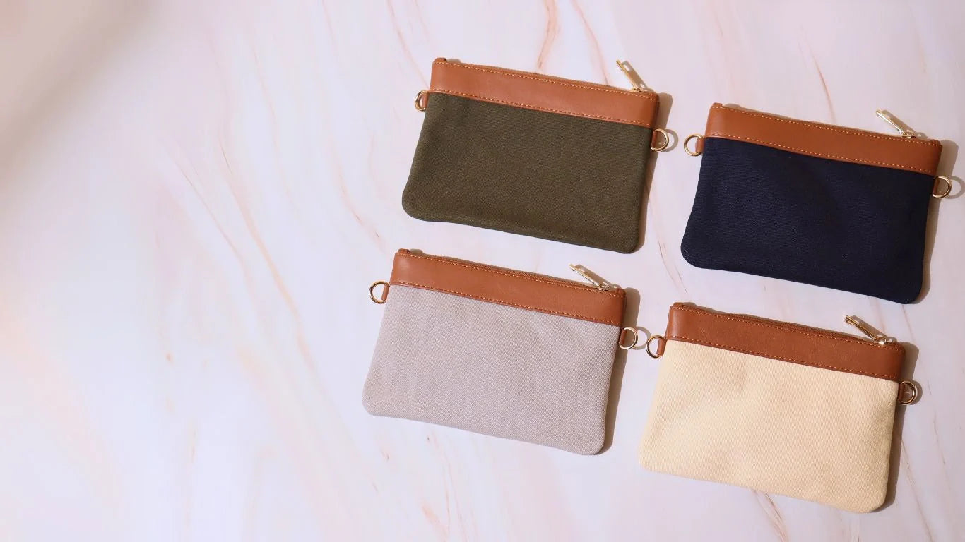 Four Canvas Sling Pouches in Dark Green, Navy Blue, Grey and Off-white on a white marble background