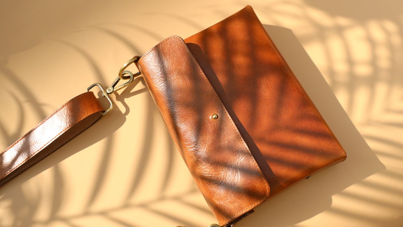 Tan Shoulder Sling Crossbody Bag in Tan Leather under the the shadow of palm leaves