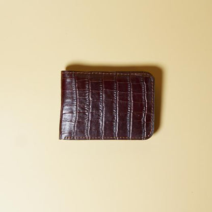 Maroon leather bifold wallet with crocodile texture on a beige background