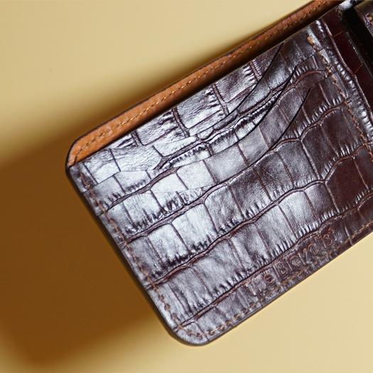 Close up detail of three card slots on a Maroon leather wallet with crocodile texture on a beige background