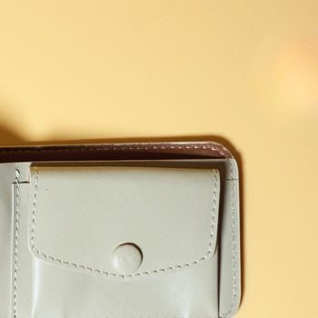 Close-up of a Off White bifold leather wallet with a leather covered button on a yellow background