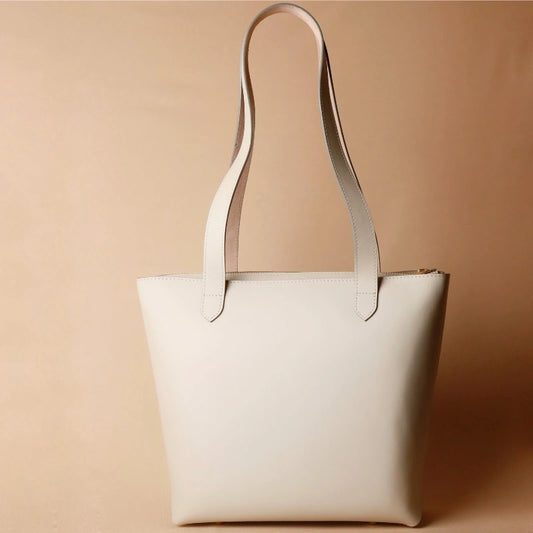 White Leather tote bag with zip on a light peach background