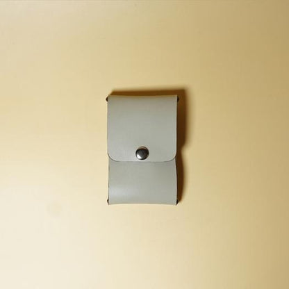 Small light gray leather card holder with a metal snap button on a beige background
