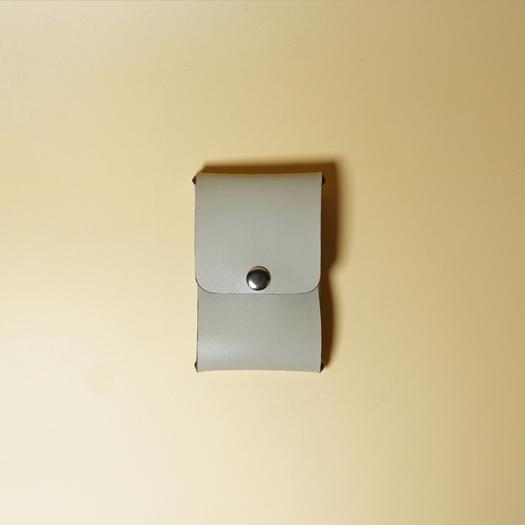 Small light gray leather card holder with a metal snap button on a beige background