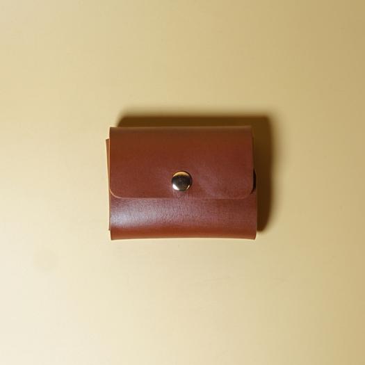 Tan Brown Leather Visting card case with a metal button on a beige background