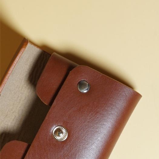 Close-up of a tan brown leather wallet with gold buttons on a beige background