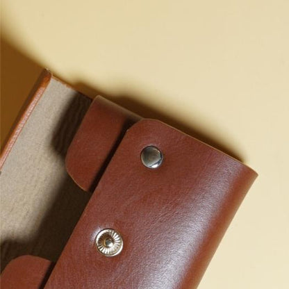 Close-up of a tan brown leather wallet with gold buttons on a beige background
