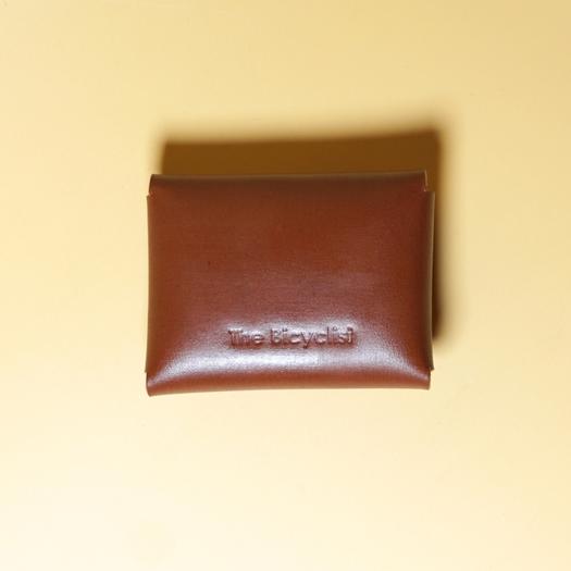 Tan Brown leather pouch with 'The Bicyclist' branding on a yellow background