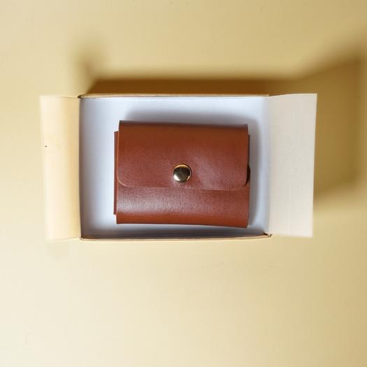 Tan Brown leather wallet in an open box on a beige background