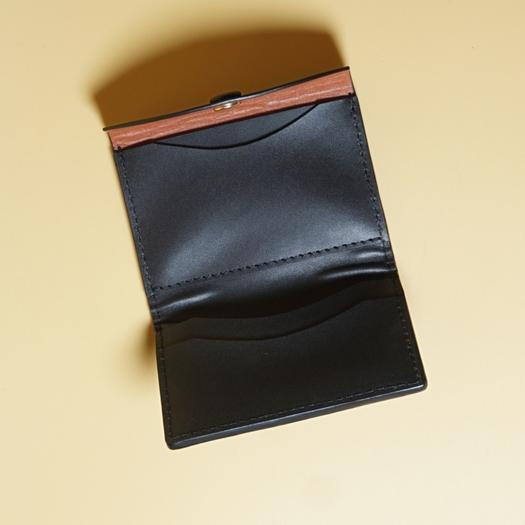 Black leather wallet with tan leather lining on a beige background