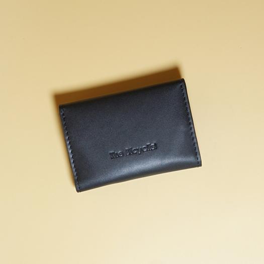 Black leather wallet with 'The Bicyclist' branding on a beige background