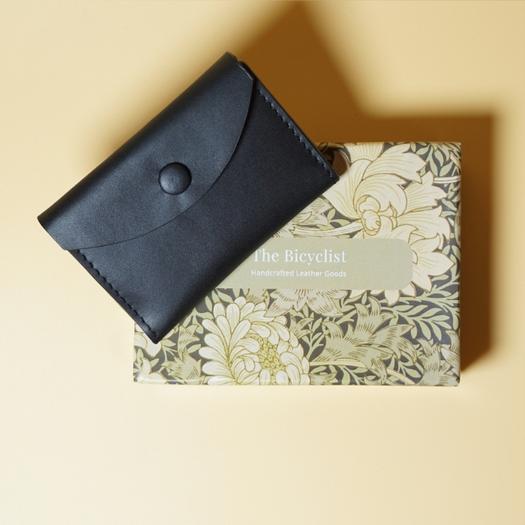 Black leather wallet and floral-patterned box on a beige background