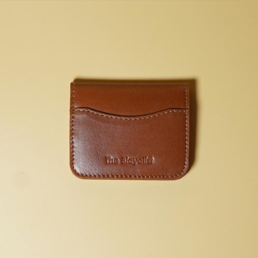 Tan leather cardholder wallet with 'The Bicyclist' branding on a beige background