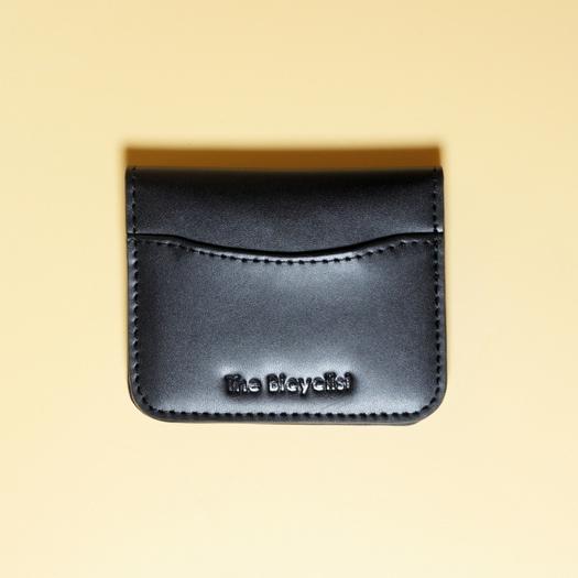 Black leather cardholder with 'The Bicyclist' branding on a beige background