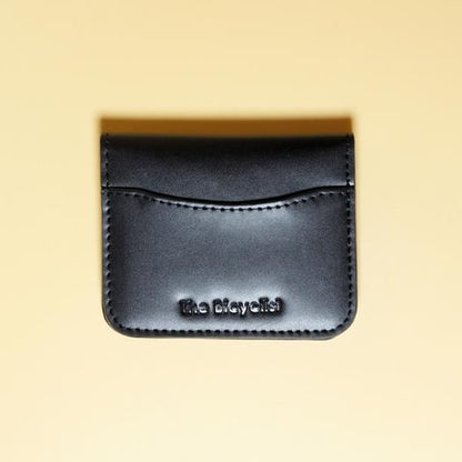 Black leather cardholder with 'The Bicyclist' branding on a beige background