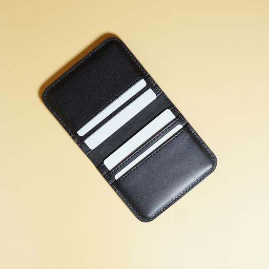 Black leather cardholder with four white cards on a beige background