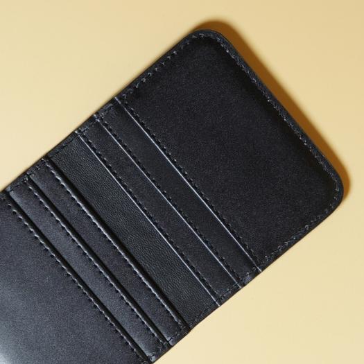 Close up view of the stitching on a Black leather wallet on a beige background