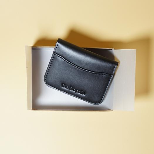 Black leather cardholder with 'The Bicyclist' branding on a light yellow background