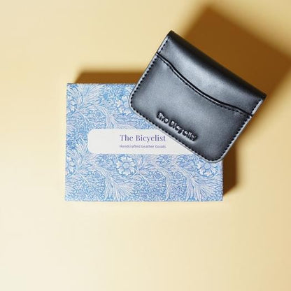 Black leather cardholder on a blue patterned box with 'The Bicyclist' branding on a beige background