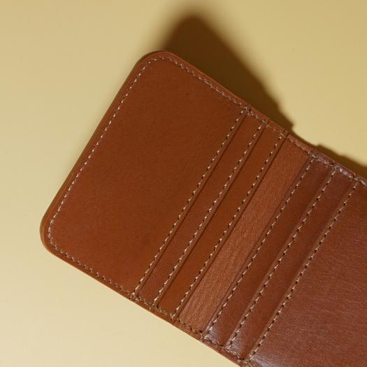 Close-up of the stiching on a tan brown leather wallet on a beige background