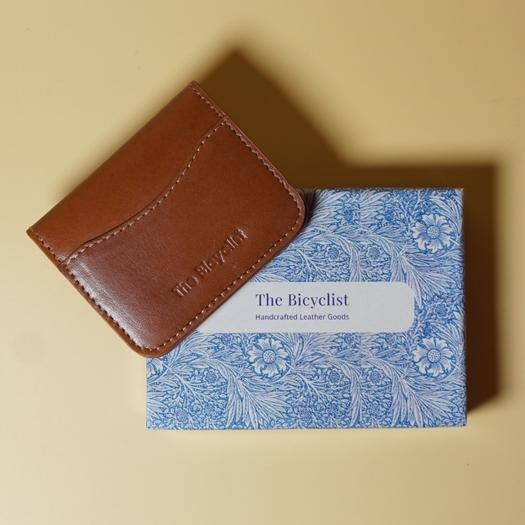 Tan Brown leather wallet on a blue patterned card with 'The Bicyclist' branding.
