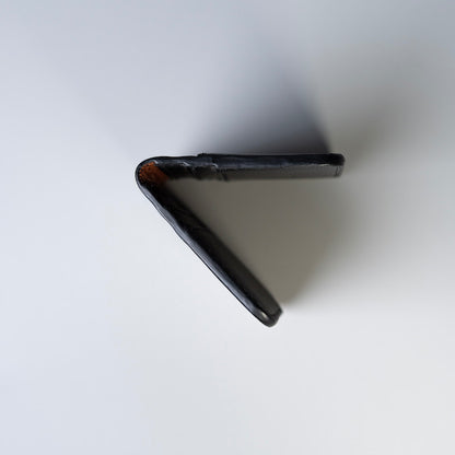 A side detail view of a black full grain leather wallet or card holder shown from an overhead angle on a plain white background.