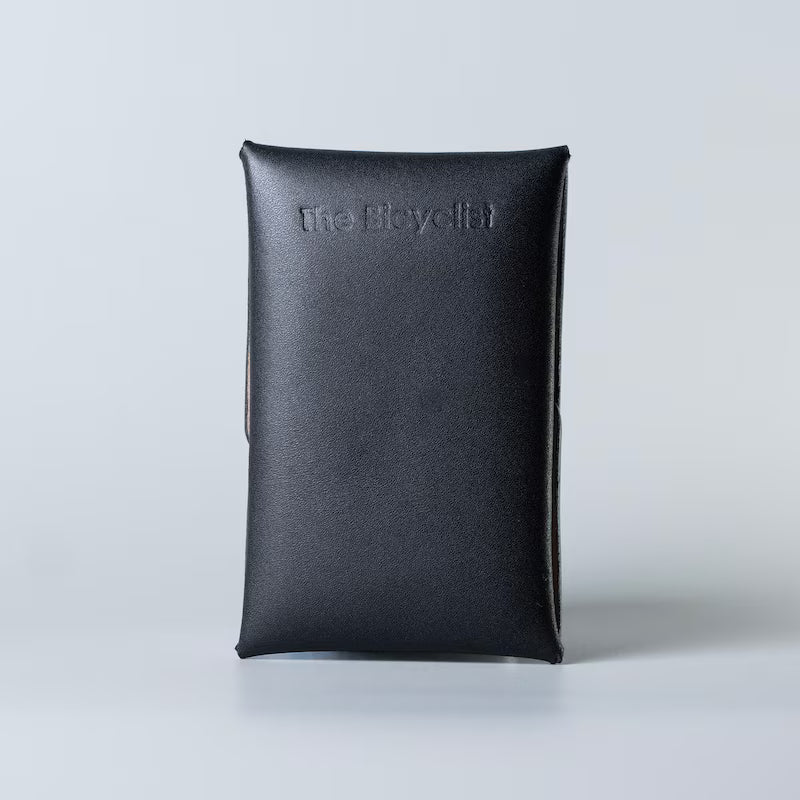 A black full grain leather card pouch or card case standing upright on a light gray background, featuring the debossed brand name 'The Bicycle' on the back.