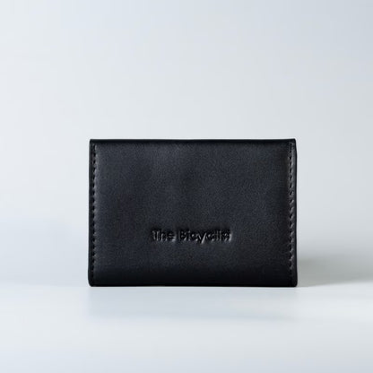 A black full grain leather card holder wallet with 'The Bicyclist' debossed on the back, set against a clean white studio background.