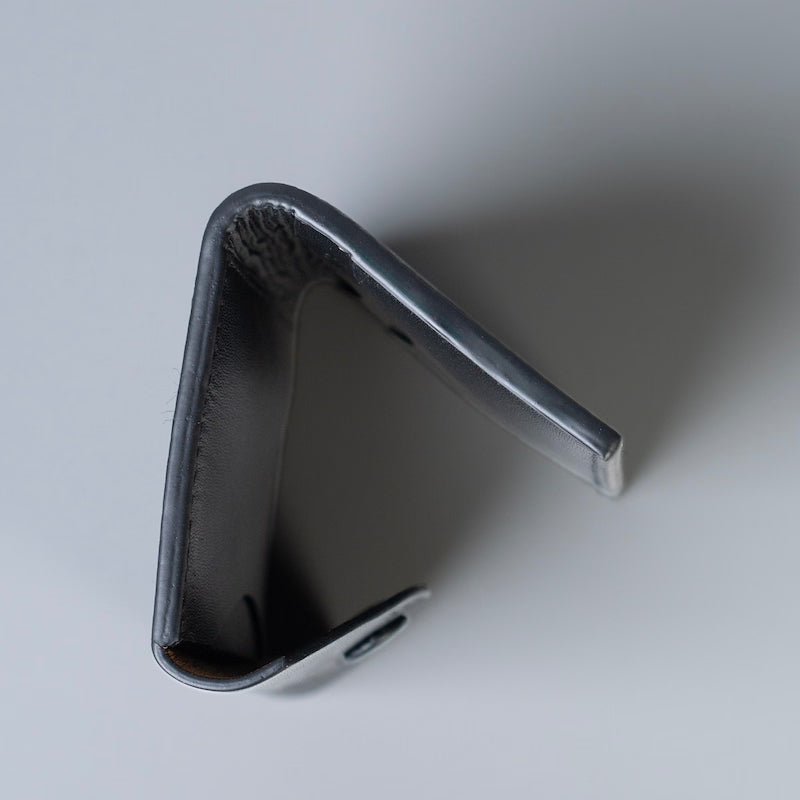 Detailed side edge view of a full grain slim bifold wallet with a flap and a snap button closure by 'The Bicyclist' on a  neutral light gray background.
