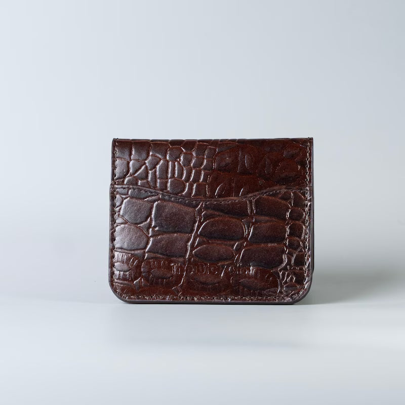 Full grain leather maroon slim bifold card wallet in corocodile leather texture with a card slot from The Bicyclist on a soft grey background 