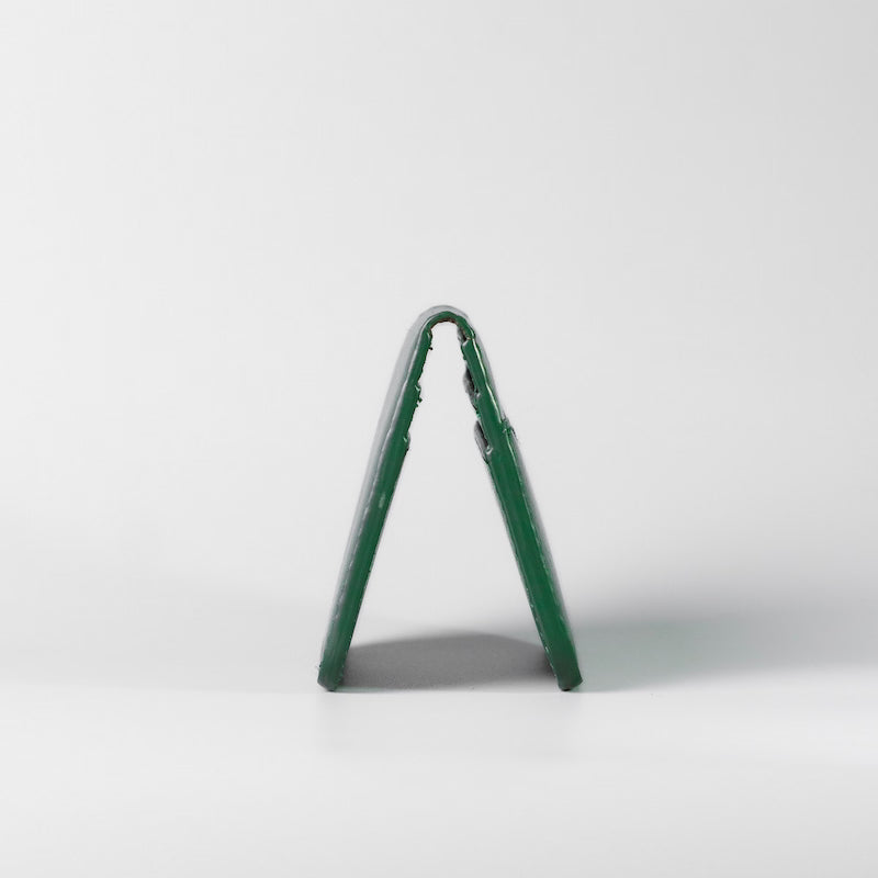A side detail image of a hand finished edge of a dark green full grain leather card wallet made by, 'The Bicyclist' on a light gray surface against a white background