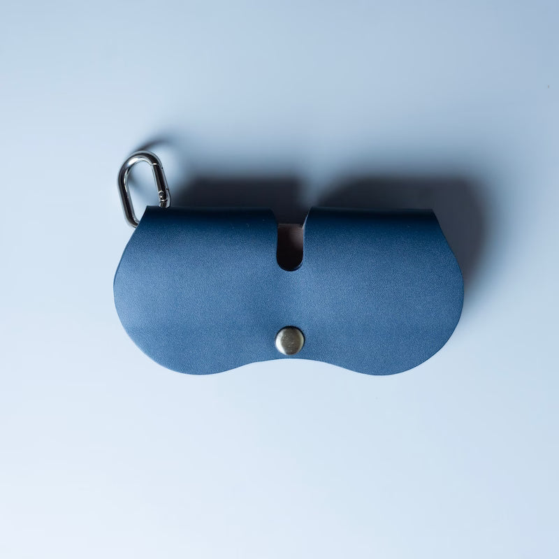 Navy blue full grain leather sunglass and spectacle case with a electroplated chrome hook and a snap button made by 'The Bicyclist' on a soft grey background